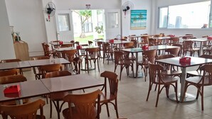 A spacious dining area with multiple tables and chairs, ceiling fans, and large windows offering a view of the outdoors. - Reserva do Sahy, Condado (Mangaratiba)