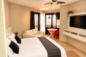 A hotel room with a bed, a sofa, a small table with chairs, a TV, and a balcony with curtains. - Reserva do Sahy, Condado (Mangaratiba)