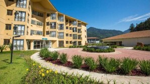 Um hotel de vários andares com um pátio, rodeado por vegetação e com uma paisagem de montanhas ao fundo.