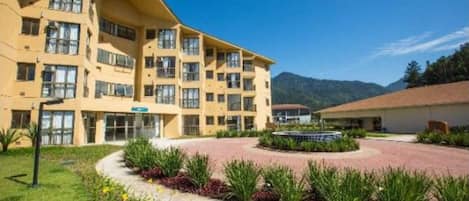 Un hotel de varios pisos con un patio interior, rodeado de vegetación y una montaña al fondo.