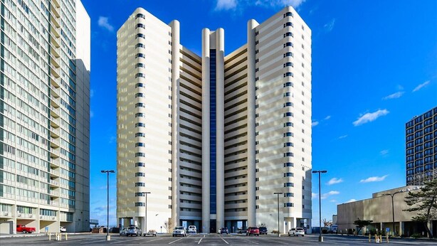 A modern building with a central atrium and multiple floors, surrounded by a parking lot. - Atlantis-2 Bedroom Ocean Front Condo with Outdoor Pool! (Ocean City)