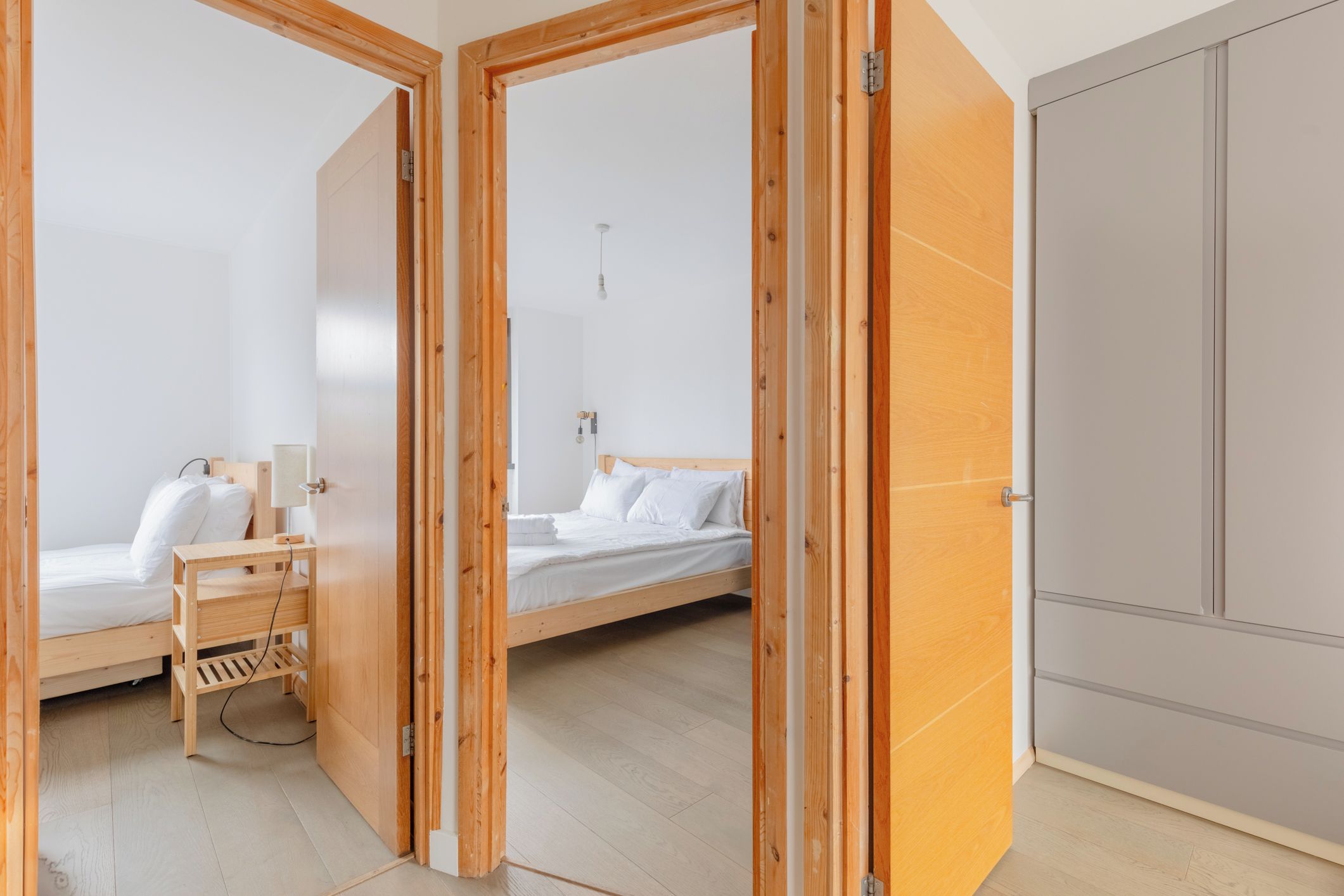 A room with two beds, a wooden wardrobe, and a bedside table.