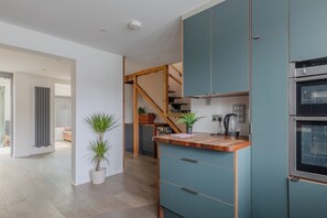 A modern kitchen with teal cabinets, a wooden countertop, and a built-in oven. - Homely and Spacious 3BD Home in Islington (London)