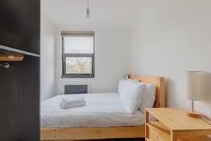 A bedroom with a single bed, a bedside table, a lamp, a radiator, and a window with a view of trees. - Homely and Spacious 3BD Home in Islington (London)
