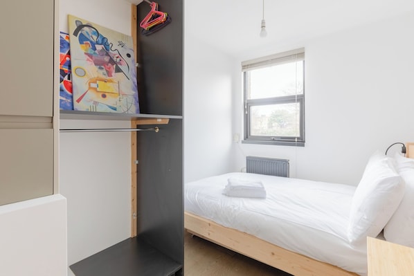 A bedroom with a bed, a radiator, a window, and a wall-mounted painting.