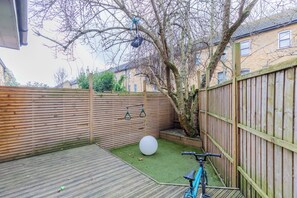A backyard with a wooden deck, a tree, a swing set, and a bicycle.