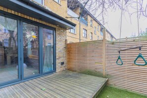 A residential backyard with a wooden deck, a sliding glass door, and a wooden fence. - Homely and Spacious 3BD Home in Islington (London)