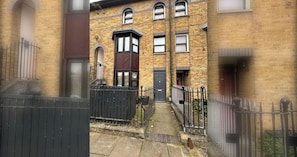 A narrow alleyway with a brick building, a black metal gate, and a small step leading to a door. - Homely and Spacious 3BD Home in Islington (London)