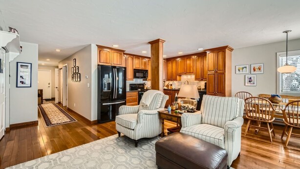 A modern kitchen with wooden cabinets, a black refrigerator, and a dining area with striped chairs and a table. - Stone Creek Meadows 205 2 Bedroom Condo (Avon)