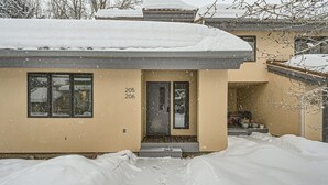 A two-story house with a beige exterior, numbered 205 and 206, surrounded by snow. - Stone Creek Meadows 205 2 Bedroom Condo (Avon)