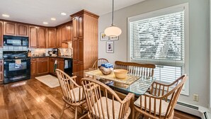 A kitchen with wooden cabinets, a black stove, and a dining table with chairs. - Stone Creek Meadows 205 2 Bedroom Condo (Avon)
