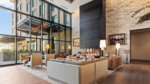 Een moderne lobby met een ruime zithoek, een open haard en uitzicht op het exterieur van het gebouw.