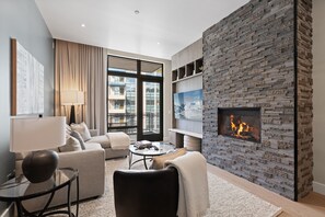 A modern living room with a fireplace, comfortable seating, and a large window offering a view of the city.