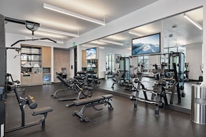 Ein modernes Fitnessstudio mit unterschiedlichen Trainingsgeräten, einem großen Spiegel und einem Fernsehbildschirm.