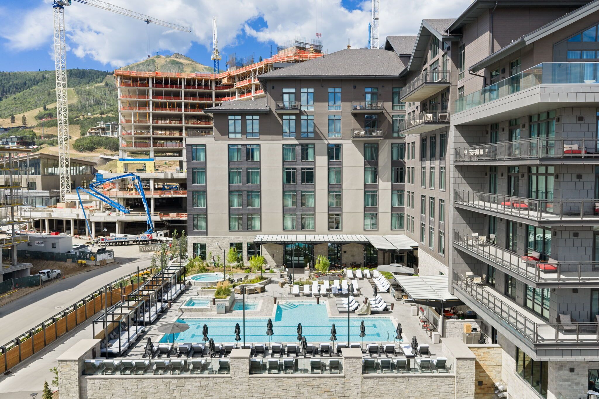 A hotel with a rooftop pool, multiple balconies, and a construction site in the background.