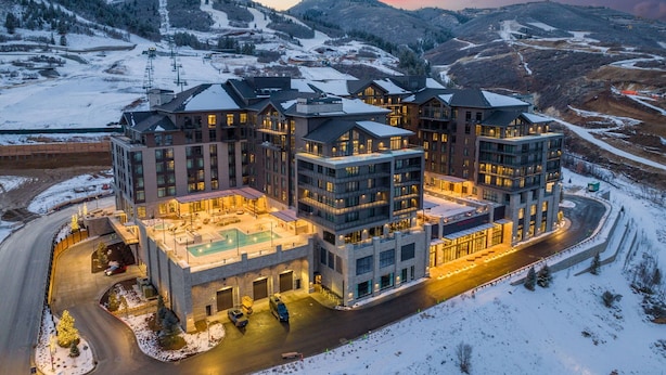 Een hotel met meerdere verdiepingen, met op de achtergrond een skipiste, inclusief een zwembad en een parkeerplaats.