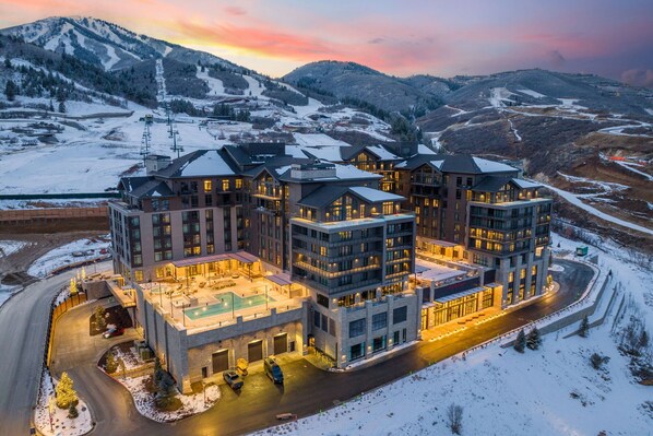 Ein mehrstöckiges Hotel mit Skipiste im Hintergrund, inklusive Pool und Parkplatz.