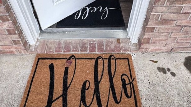 A white door with a 'Welcome' sign above it, a black doormat with 'Hello' written on it, and a brick wall. - Comfy 2BR 1BA Apt (Nederland)