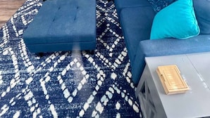 A modern living room with a blue sectional sofa, a matching ottoman, a patterned rug, a small side table, and a wall-mounted abstract painting. - Comfy 2BR 1BA Apt (Nederland)