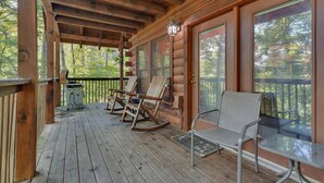 A wooden deck with rocking chairs and a metal table, surrounded by glass doors and windows. - Chillin N Grillin 2 Bedroom Cabin (Sevierville)