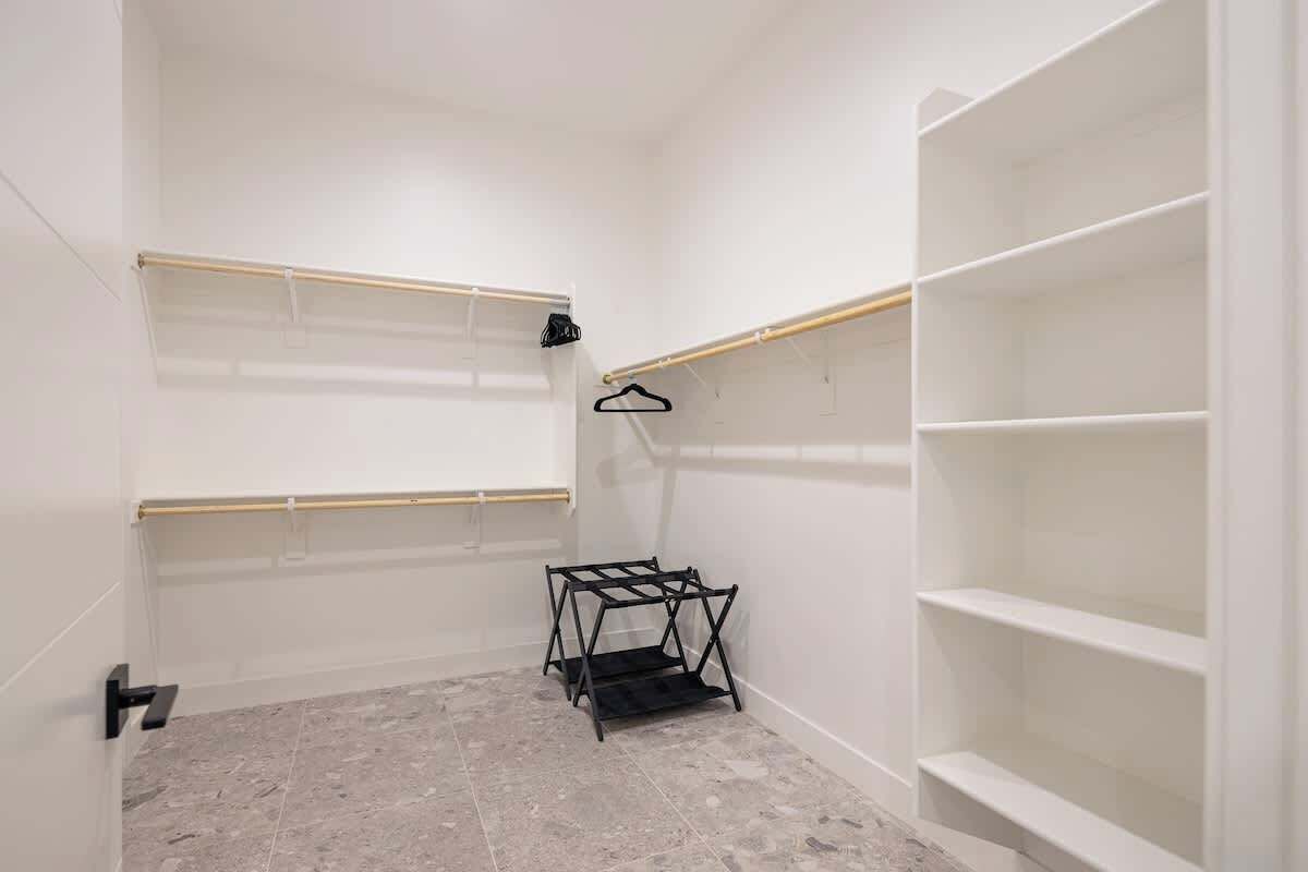 A room with white walls, a tiled floor, and a black metal rack with shelves.