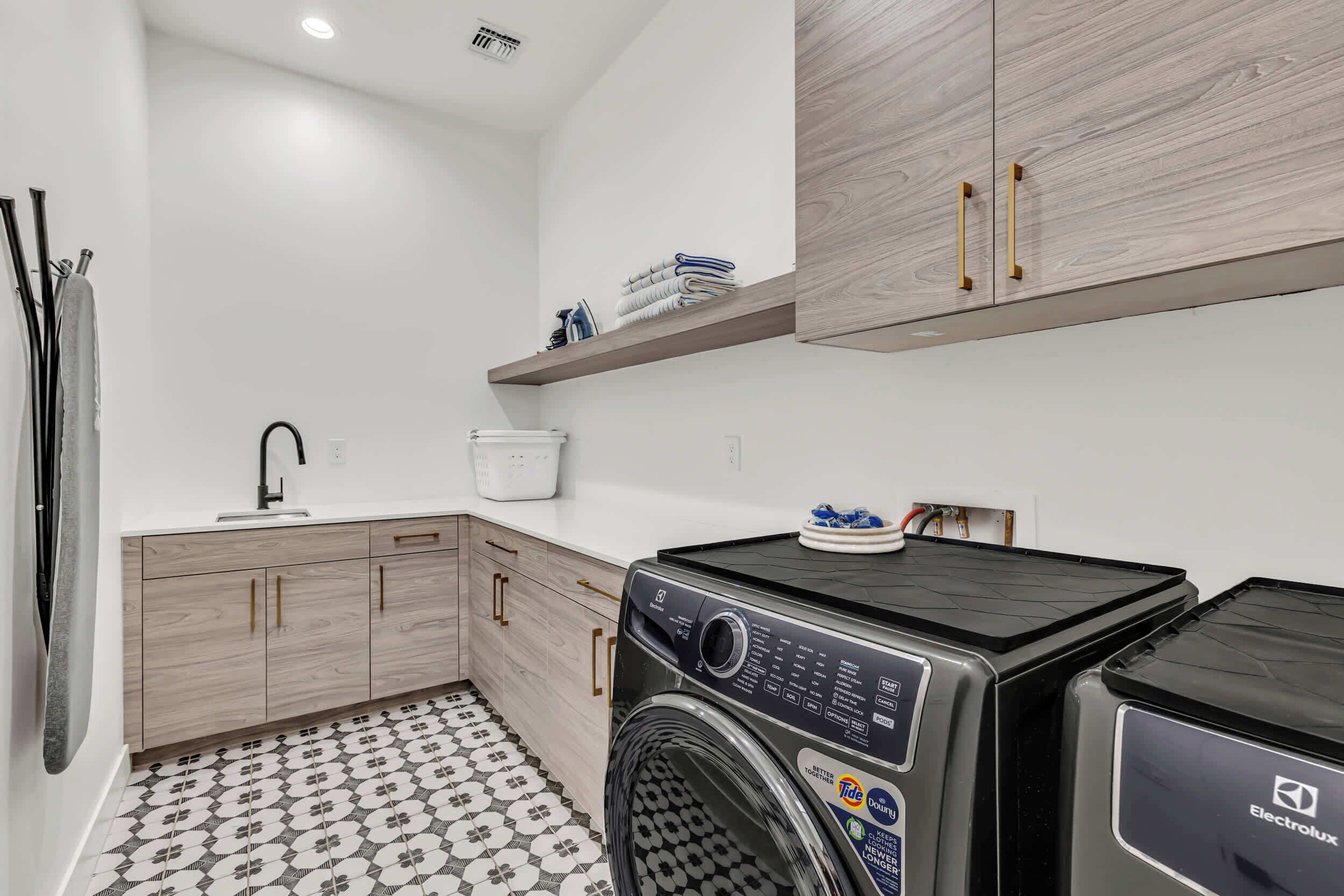 A modern laundry room with a washing machine, dryer, and wooden cabinets.