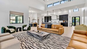 A spacious living area with a large sofa, a coffee table, and a patterned rug. There is a kitchen area with modern appliances and cabinets. - Luxury Lounge - 5BR, Pool&Spa, Sauna, Firepit (Scottsdale)