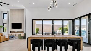 A modern living room with a large wooden dining table and black chairs, a flat-screen TV mounted on the wall, and a fireplace. - Luxury Lounge - 5BR, Pool&Spa, Sauna, Firepit (Scottsdale)