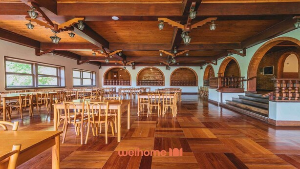 Ein geräumiger Speisesaal mit Holztischen und -stühlen, gewölbten Backsteinwänden und einer Holzbalkendecke mit hängenden Laternen.