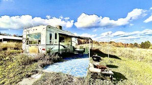 A vintage RV parked in a grassy field with a blue-tiled patio and a small table with a bowl.