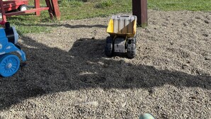 A playground with swings and a small yellow toy truck on gravel.