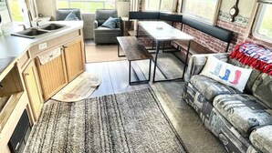 A compact RV interior with a kitchenette, seating area, and a window providing a view of the outdoors.