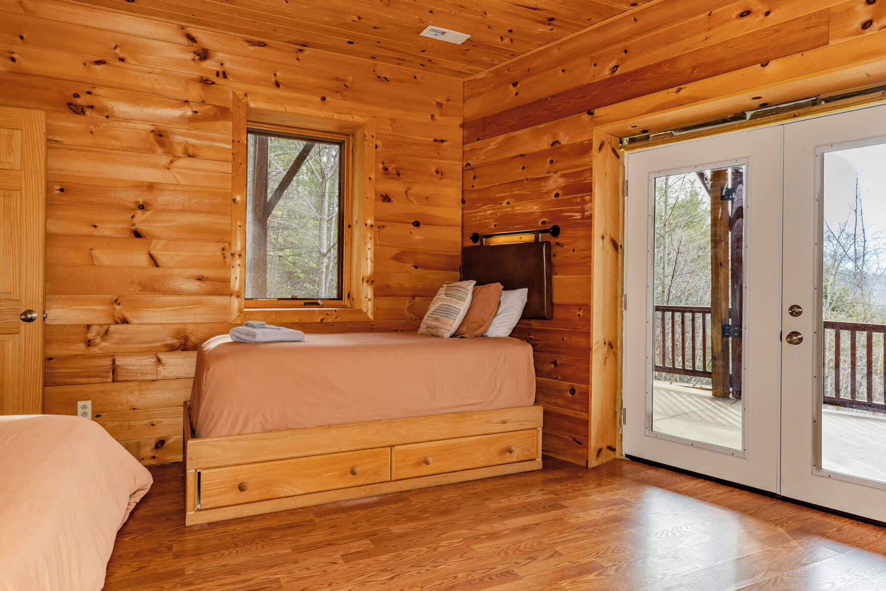 A wooden cabin bedroom with a bed, a nightstand, and a window.