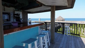 Une terrasse en bois avec un bar, des tabourets et une vue sur l’océan.