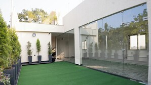A modern building with a glass facade, a green artificial lawn, and potted plants. - ARK Hotels (Ranchi)