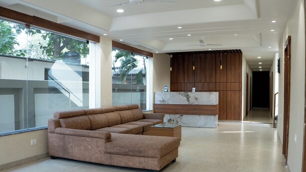 A modern living area with a sectional sofa, a marble accent table, and a wooden reception desk. - ARK Hotels (Ranchi)