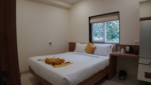 A neatly arranged bedroom with a bed, bedside table, and a window with a view of greenery. - ARK Hotels (Ranchi)