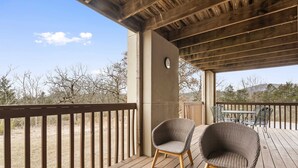 A wooden deck with two wicker chairs, a table, and a clock on a wall.