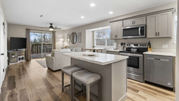 A modern kitchen with a central island, stainless steel appliances, and a sliding glass door leading to a balcony.