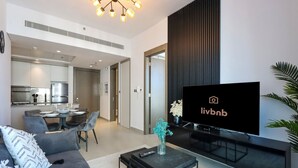 Ein modernes Wohnzimmer mit Flachbildfernseher, einer Couch, einem Couchtisch und einem Essbereich im Hintergrund.