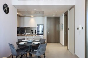 A modern kitchen with white cabinets, a stainless steel refrigerator, and a dining area with a table set for two.