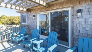 A covered outdoor seating area with Adirondack chairs and a table, wooden walls, and a sliding glass door. - Pool, Phenomenal Sunsets Await, Dogs Welcome, Spacious, D0101 (Duck)