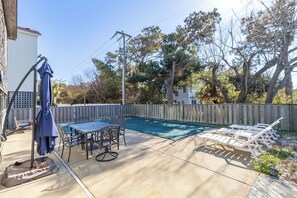 A backyard with a swimming pool, a patio table with chairs, and a deck with lounge chairs.