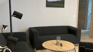 En moderne stue med en sort sofa, et rundt træbord og en gulvlampe.