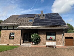 A house with a tiled roof, solar panels, a brick facade, and a front entrance with a bench. - zwEIFELlos - the vacation apartment (Monschau)