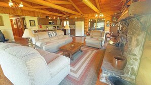 A cozy log cabin interior with a fireplace, wooden beams, and a living area with sofas and a coffee table. - 12 Mile Ranch (Custer)