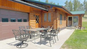 A log cabin with a garage, a patio with a table and chairs, and a small porch area. - 12 Mile Ranch (Custer)