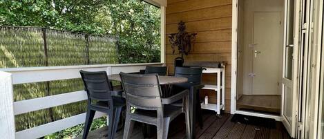 A covered outdoor area with a table and chairs, a white railing, and a door leading to an interior space.