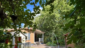 A wooden playhouse with a slide, surrounded by trees and a brick patio.