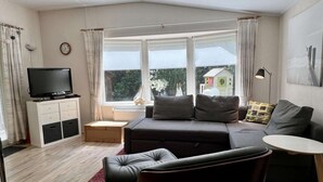 A modern living room with a sofa, a TV, a small table, and a window with curtains.